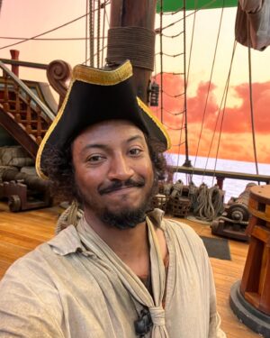 Samba Schutte Instagram - Today’s (Our) Flag (Means Death) Day, and many of you have asked for deets on my character Roach in Season 2🪳 Here you are🏴‍☠️ 
Details on the costumes during fittings and after weathering and aging. It was great collaborating with Costume Designer Gypsy and being able to implement my own backstory. For the Red Flag fit I wanted him to have a headband because a chef never gets hairs on his meals. Unless it’s on the menu, or you’re serving the British👨🏾‍🍳
For his new fit, Roach got to have more jewelry this season because he became a better pirate. I chose 3 rings. The Lion to symbolize the Atlas Mountains where he hails from. The 2 headed Snake, because you have to always watch your back as a pirate. And a Celtic looking ring, because Roach has a tender spot. Like with his mother’s scarf. And of course his talisman necklace that he always wears, with every costume🪬At first it was gonna be a long sleeve shirt, but Jenkins wanted me to show off my sexy dessert making arms. Rightly so…..💪🏾
On his belt he had meat hooks, his cleaver as a weapon and of course, a wooden spoon for self defense🥄
I’ve never worn Doc Martens before and let me tell you, I don’t know how people smaller than me do it, those things weigh a ton each! Now imagine running on the beach in them👀
More deets in stories but I loved every minute of dressing up as and playing this chaotic dude🫶 
#ourfladmeansdeath #ofmd #ofmdseason2 #roach #cosplay #bts