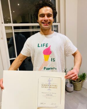 Sebastian de Souza Instagram - Dear Souzles!!! THE ENSEMBLE of @thegreathulu have been nominated for a @sagawards in the category of “silliest group of actors collected for the purposes of making a TV show in the year 2020”! 

And apparently, even if you’re just a very tiny part of the very large and very talented group of hard-working luvvies that make up an “ensemble”, @sagaftra sends you a letter on terrifically posh, bordered, glossy paper with your name on it! Every single silly one of us! 

And I’m feeling extremely proud of mine because it’s the first time I’ve been given a certificate for anything since coming third in the egg and spoon race in sports day at nursery, aged 3. Indeed, SAG’s certificate is very nearly, almost as nice as the one I got from Brightwalton Nursery c. 1996. 

AND THERE’s SOMETHING ELSE THAT MAKES THIS A VERY IMPORTANT PHOTO: I bought the really cool “Life Is Fantastic” T-Shirt I’m wearing from my best mate Tommy’s shop @zigzag.clothing , which is the only place on the internet that sells TRULY ACTUALLY COMFY 100% SUSTAINABLE AND VEGAN CLOTHING!!! Get yours there now! And #savethefuture whilst you’re at it! 

Thank you Tommy @zigzag.clothing ! Thank you SAG @sagaftra ! THANK YOU SOUZLES!!! 

And well done @ellefanning @nicholashoult @sacha_dhawan @phoebemercedes @charitywakefield @louis.hynes @mrgwilymlee @thebelindabromilow @florencekeithroach @gbadamosi @danusiasamal @christophe.tek @jamiedemetriou #DouglasHodge #AdamGodley (amongst many talented others!!!)