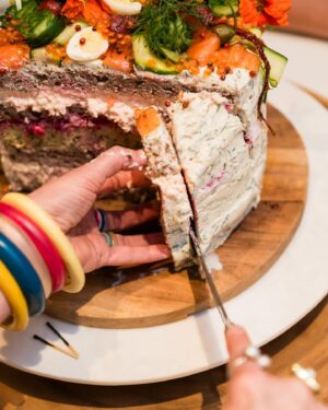 Annabel Crabb Instagram - Beautiful birthday celebration this weekend for my lovely friend @fionahughes3, a warm hearted, modest, funny, super competent general delight of a person. Also does not like sweet things so an intriguing birthday cake challenge. This one, concocted in collaboration with @glamgwenblake and modeled on the Swedish concept of Smorgastorte (or sandwich cake, and yes there are many umlauts and whatchamacallits missing from my reference) involves several large miche loaves from @goodwoodbakeshop from which rounds of bread were extracted like those arctic ice plug things, and layered with:
Salmon rillettes (hot smoked)
Zucchini and dill frittata
Beetroot pate
Tarama whipped w cream cheese.
Toppers: Cucumber ribbons and carved flowers, quail eggs, radish flowers, caper berries, horseradish and dill cream, pink pepper corns, salmon roe, candied baby beets, gone-to-seed herbs and nasturtium flowers from our primary school’s kitchen garden (stolen under cover of Book Week), also smoked salmon.
Thank you to our Scandi friends for being such sickoes as to normalise cakes made of fish. Also please enjoy my teenage son’s highly skeptical response on having the concept outlined.
Most importantly: Happy birthday to a good, good woman. ❤️ 
(And as usual thanks to @mr_stephenblake for photography, well the good photos anyway)
